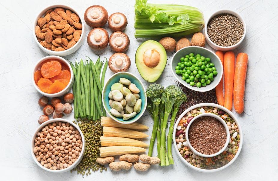 Assorted plant-based foods including nuts, seeds, beans, vegetables, and grains on a white background