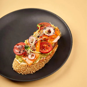 Plant-based open sandwich with avocado, tomato, sprouts, and sesame bread on black plate