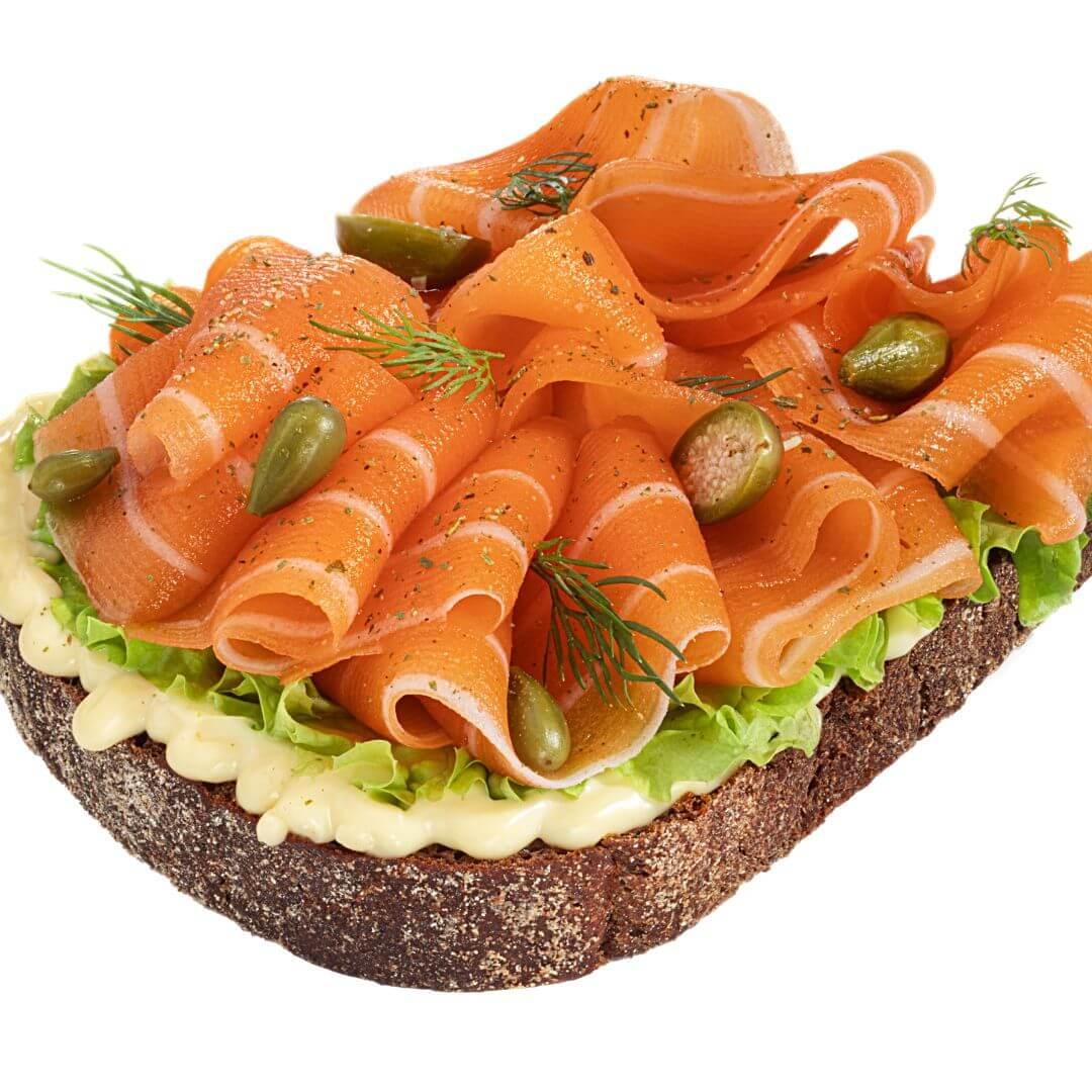 Open-faced plant-based smoked salmon sandwich with lettuce, capers, dill, and creamy spread on rye bread