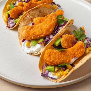 Three plant-based tacos with crispy nuggets, corn, purple cabbage, and fresh herbs on a plate
